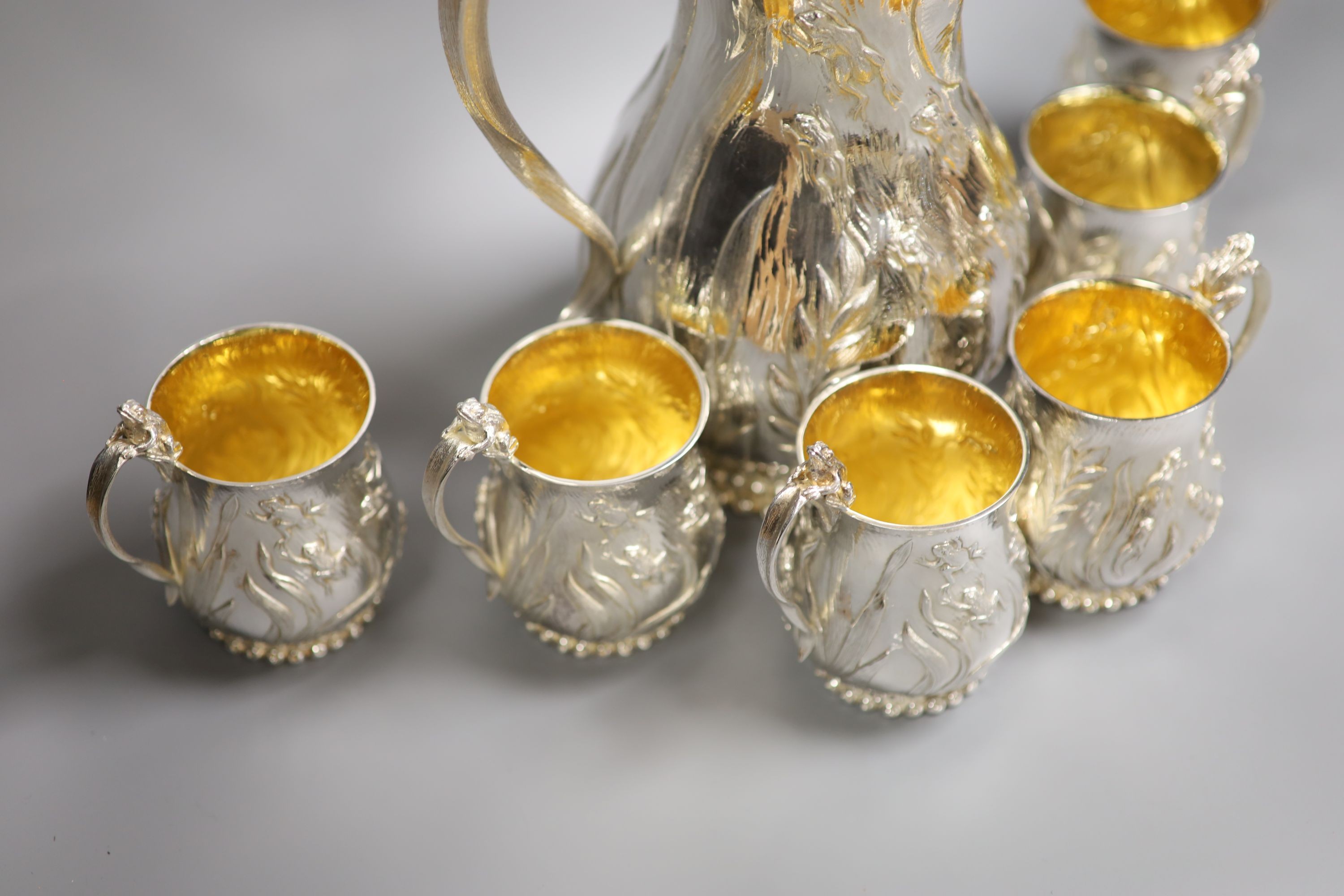 A good set of six Garrard & Co Ltd silver mugs and a matching jug, London, 1997, all embossed with frogs spawn amongst reeds, with gilded interiors, jug height 27.1cm